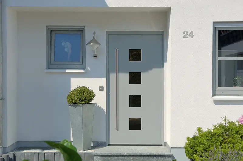 Graue Haustür mit vier Glasausschnitten und Edelstahlgriff an einem hellen Einfamilienhaus